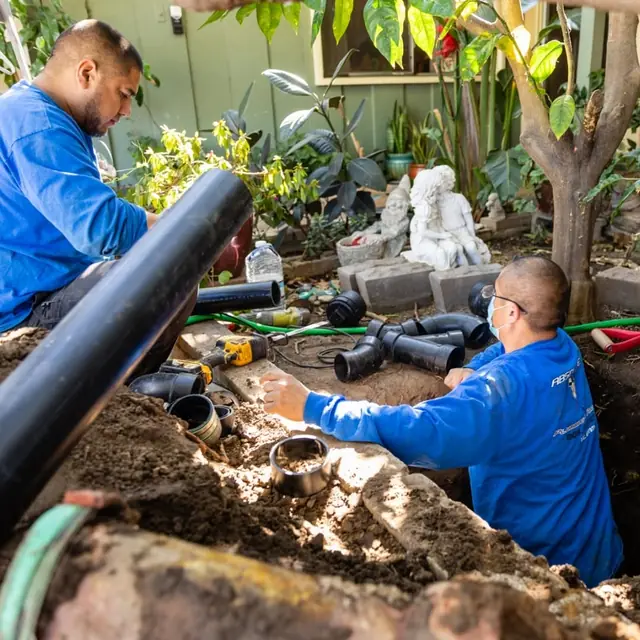 Two Absolute Plumbing technicians installing pipe in a backyard trench